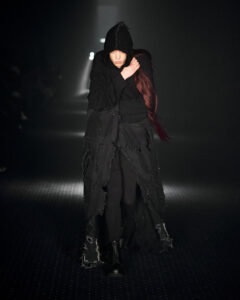 Model walking for P.L.N wearing long black coat with hood during Copenhagen Fashion Week AW23