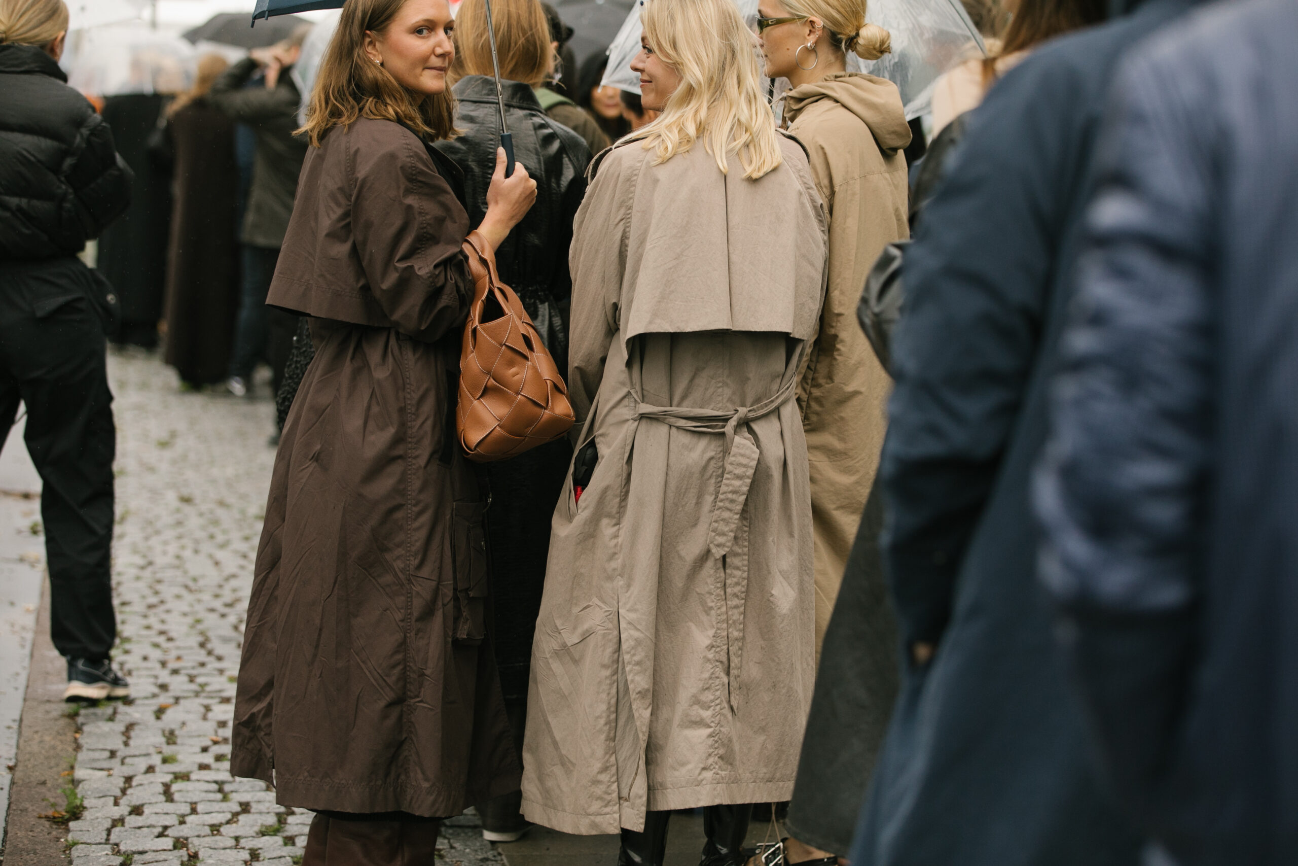 kvinder i trenchcoats i brune og beige nuancer stående i menneskemængde
