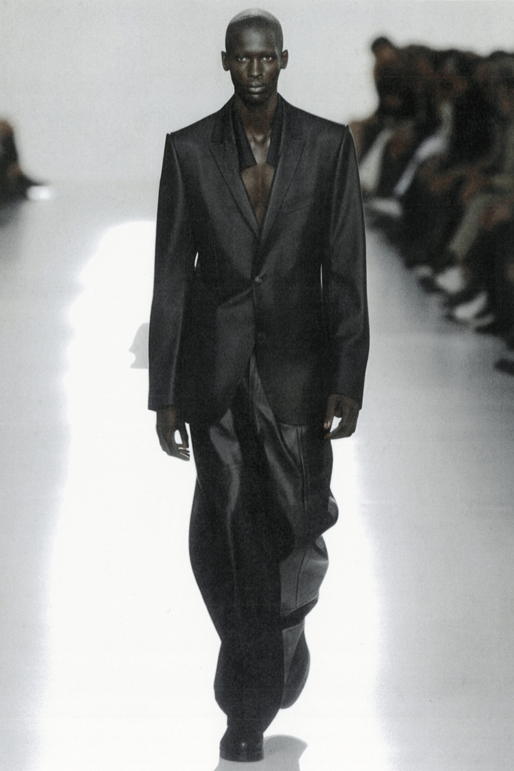 Model iført Heliot Emil sort skinnende jakkesæt under Paris Fashion Week SS24 brugt AI